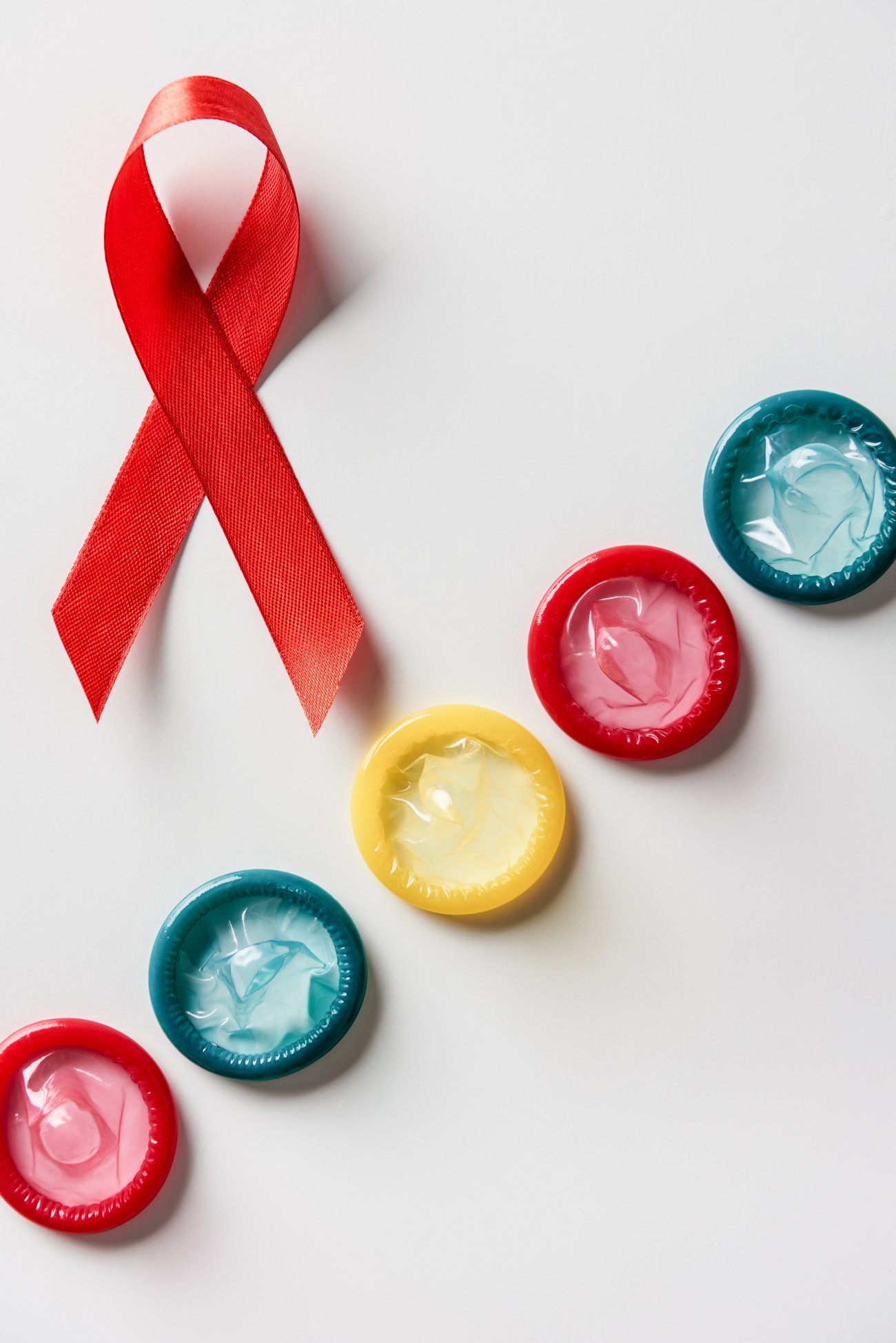 vue de dessus d'un ruban rouge de sensibilisation au sida et de préservatifs multicolores sur fond blanc