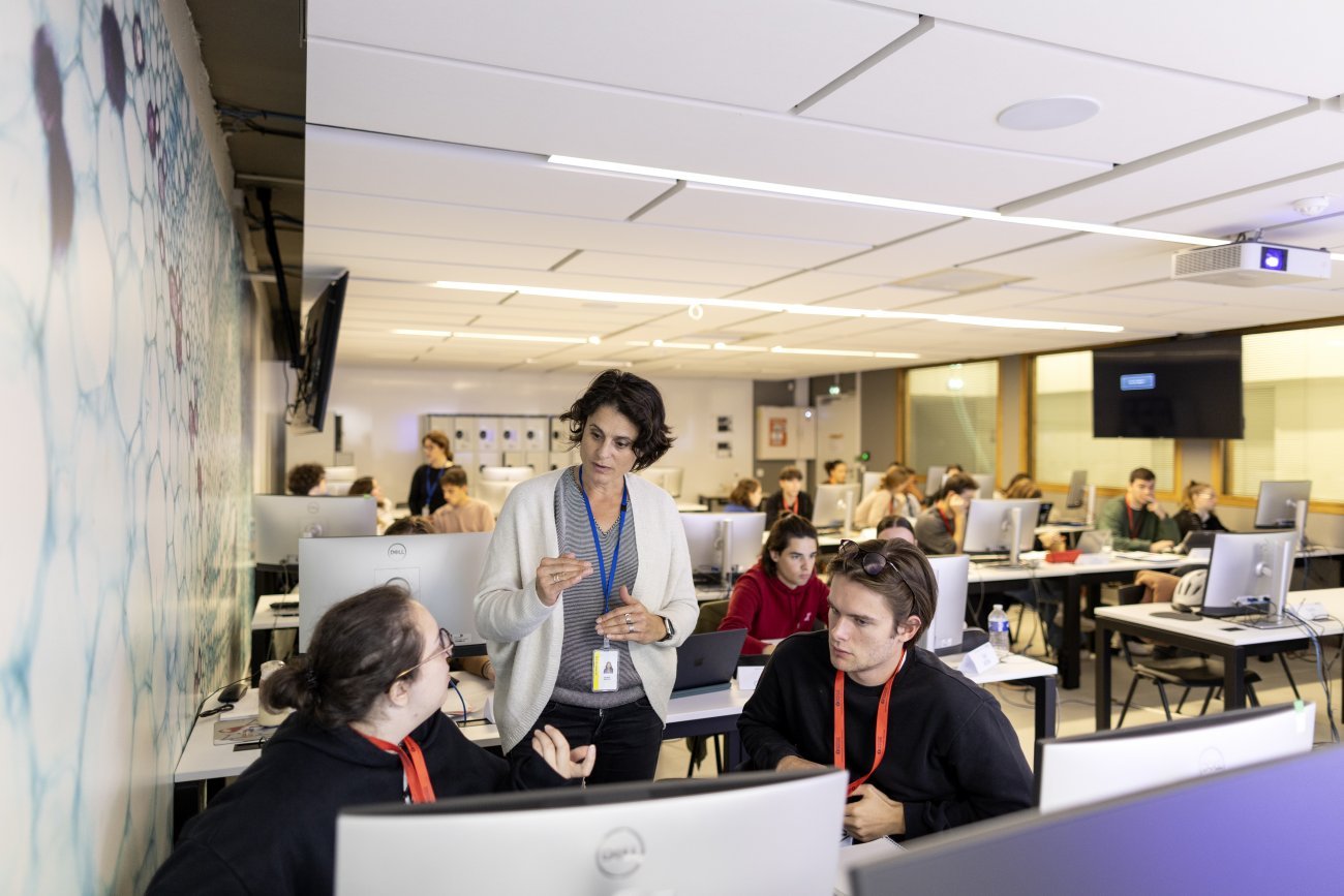 Salle de classe avec ordinateurs, élèves et professeur discutent